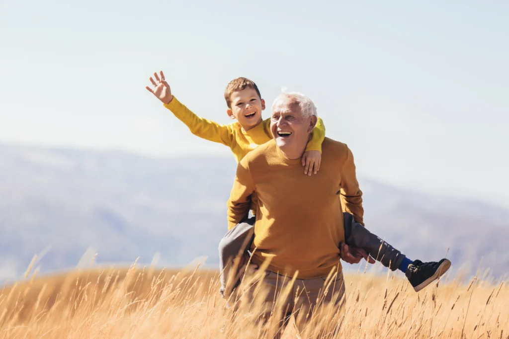 Grandfather and grandson joyfully embracing longevity and vitality in a field.