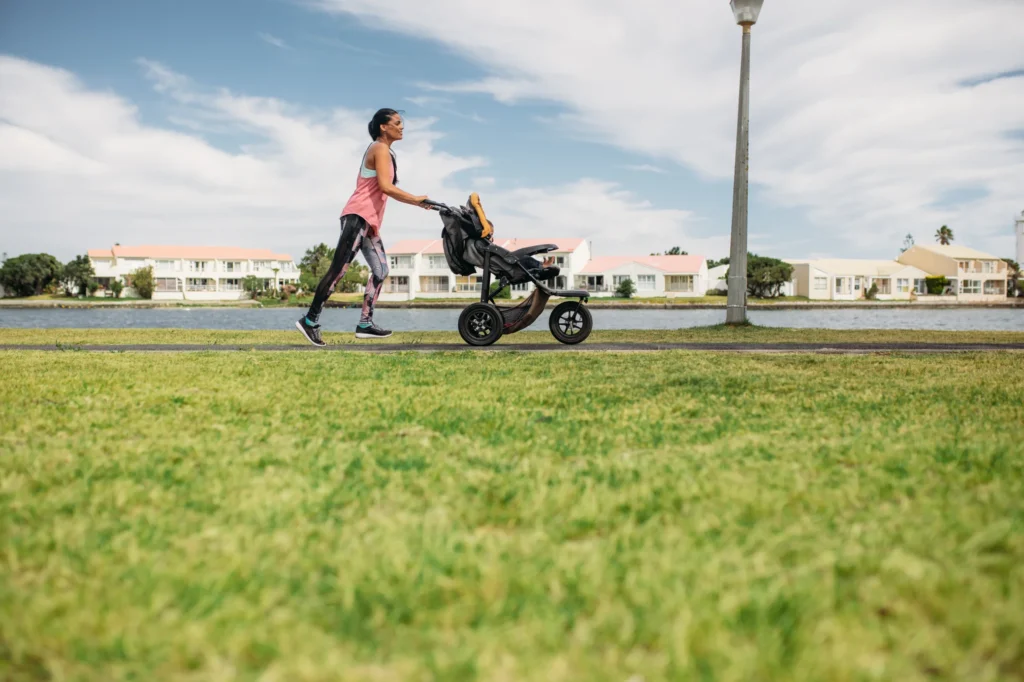 Woman walking energetically with a stroller along a waterfront path, embodying longevity and vitality.