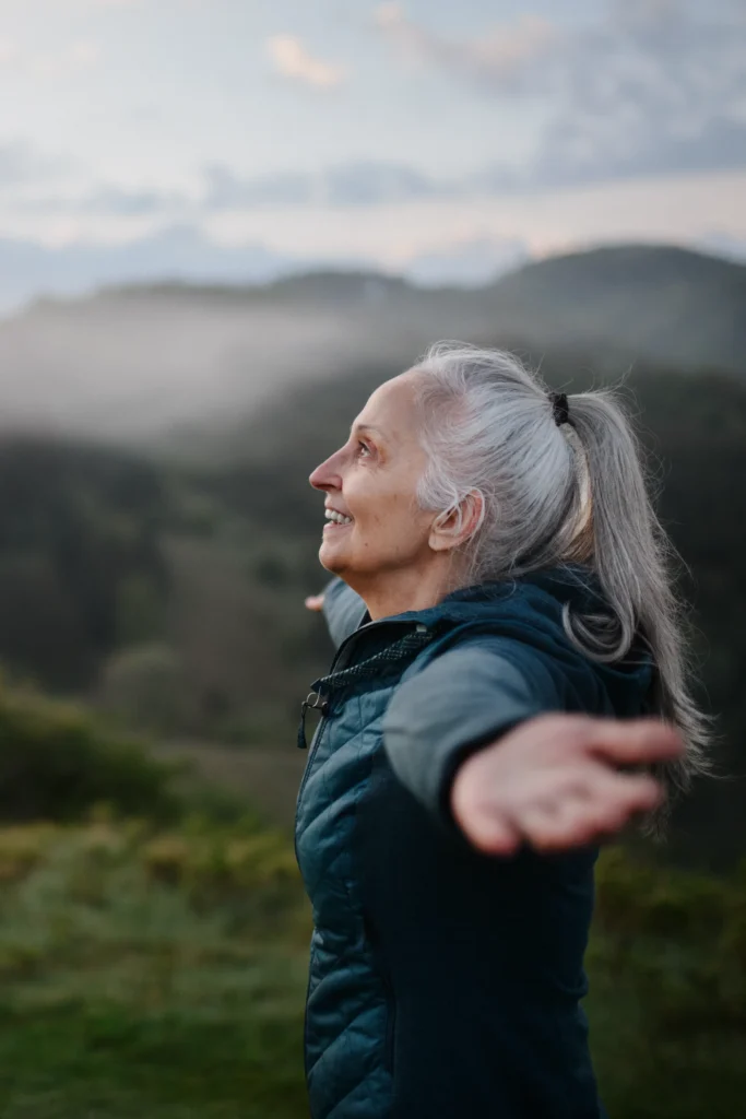 Elderly woman embracing nature with open arms, embodying vitality and energy.