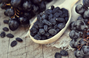 Wooden spoon filled with dried black currants surrounded by fresh grapes, highlighting energy and wellness.