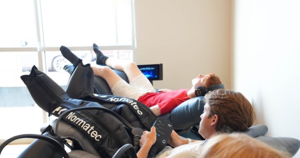 Three clients receiving Normatec compression therapy in reclining chairs at Sisu Longevity Studio in Colorado Springs, one adjusting the controller